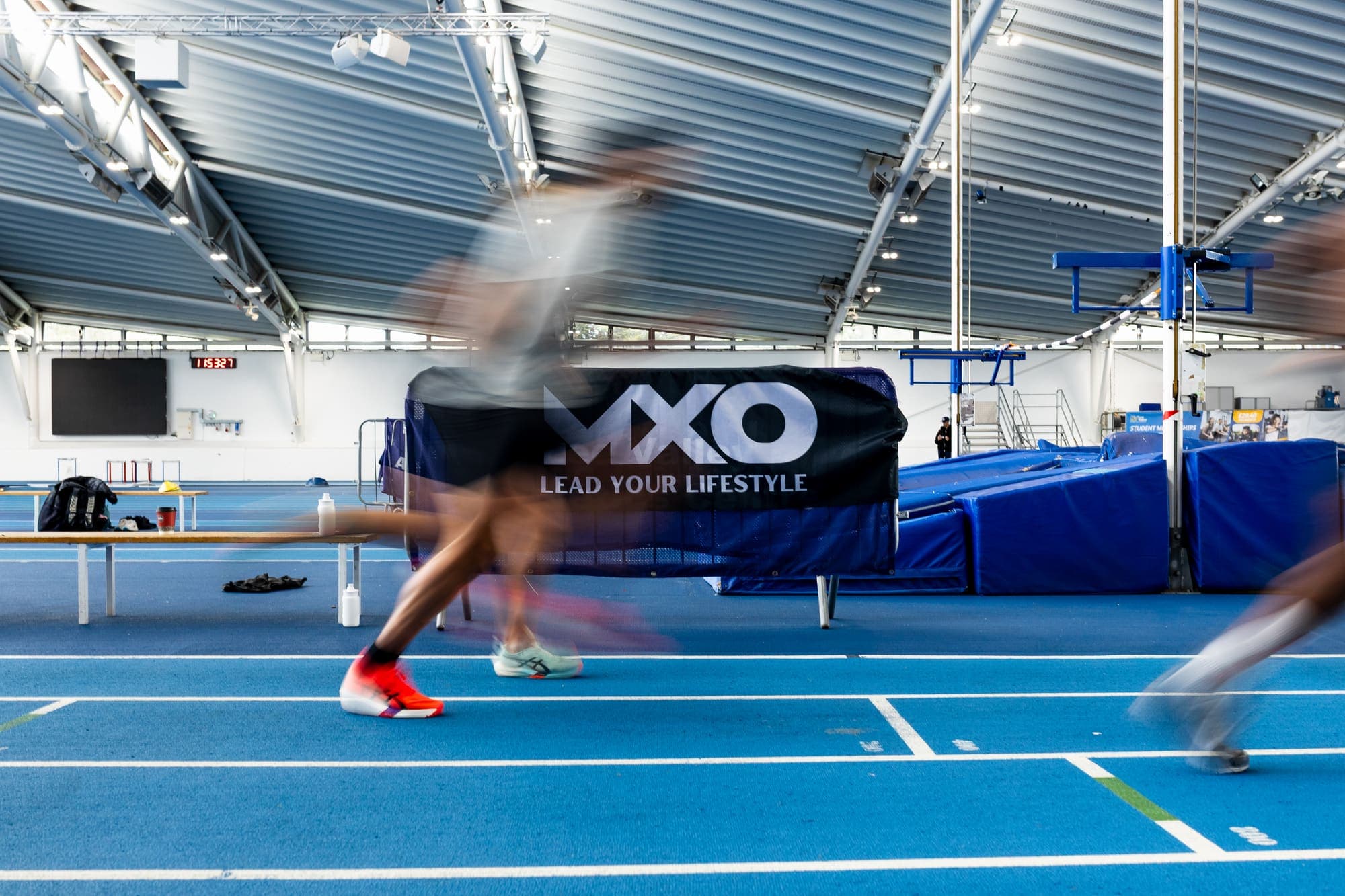 Runners mid-session on an indoor track beside an MXO banner
