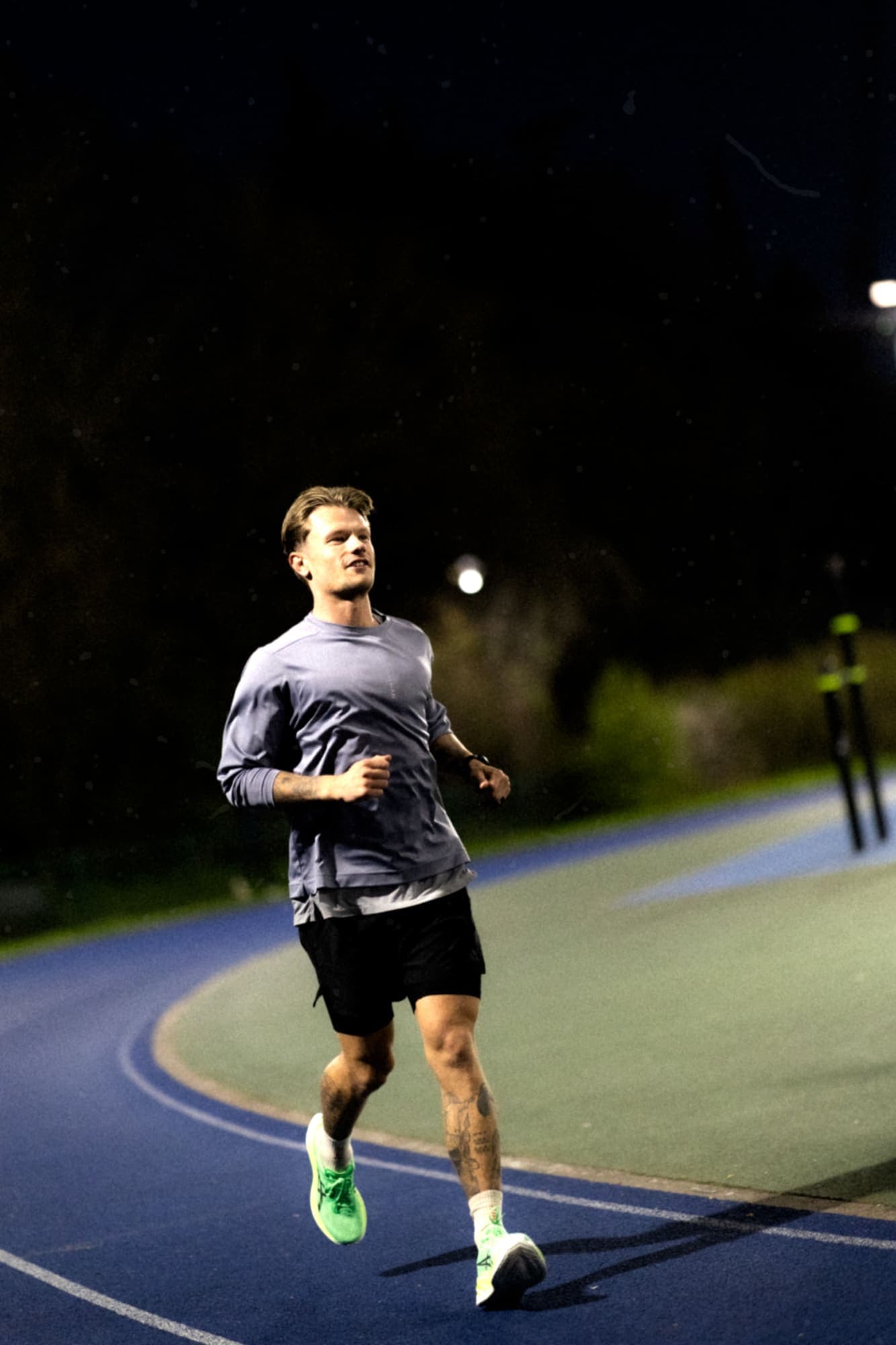 A runner training alone on a floodlit track at night