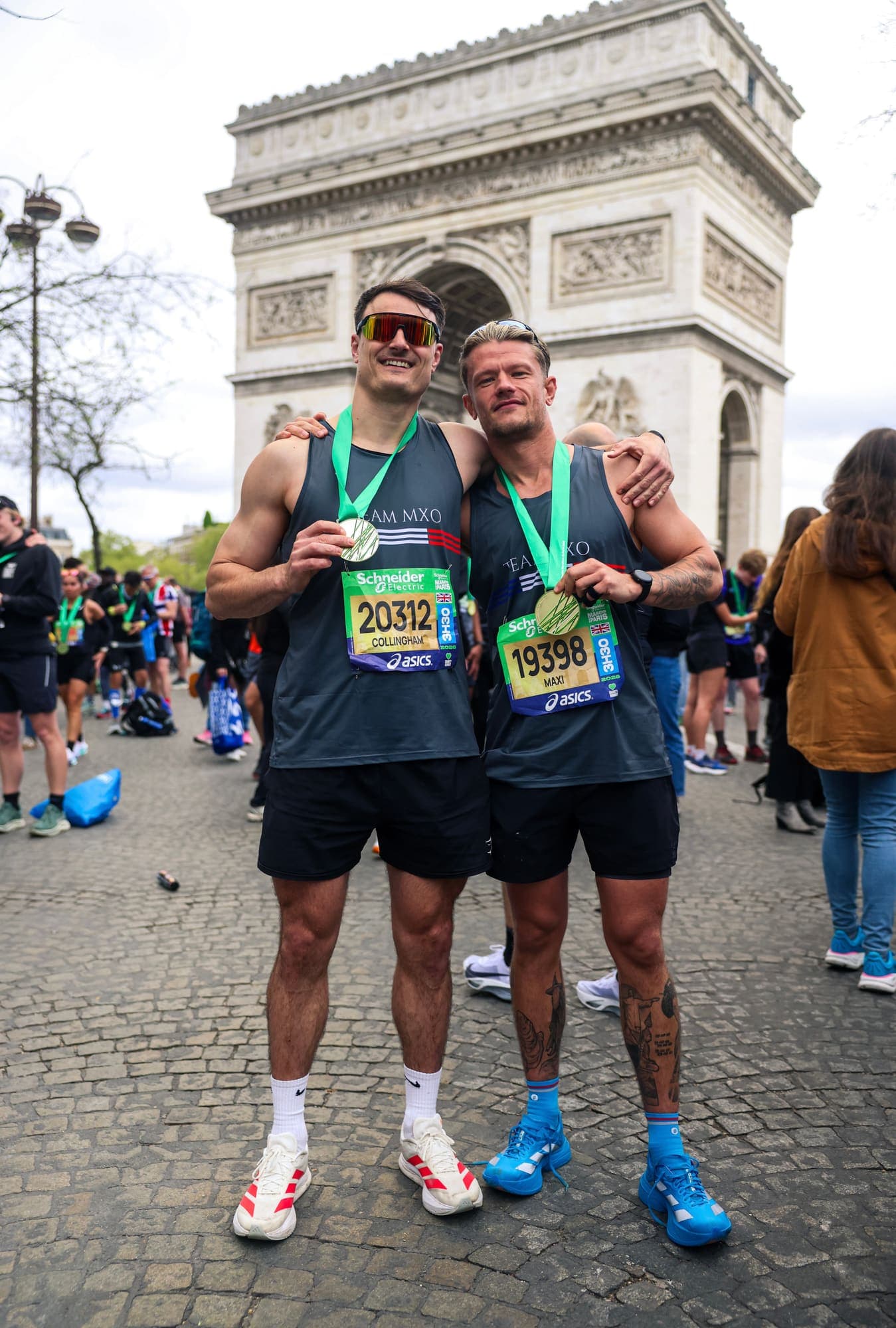 Two Team MXO runners with their finisher medals in front of the Arc de Triomphe after the Paris Marathon
